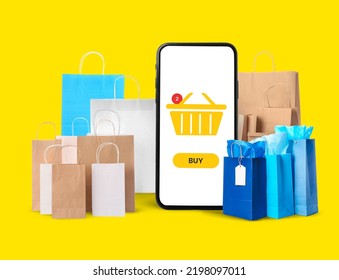 Big Smartphone And Many Paper Bags On Yellow Background. Online Shopping Concept