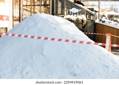 A big snowdrift, a pile of uncollected snow. Striped red and white signal tape encloses a place for cleaning on the street. Municipal service in the city. Moscow, Russia.