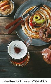 Big Spiral Fried Sausage, Meat Snacks Wienerwurst, Ham, Marinated Chili Peppers Served In Salted Pretzels And Plate With Glass Of Lager Beer And Mustard Over Dark Wooden Background. Top View