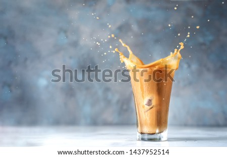Big splash in glass of cappuccino on blue background