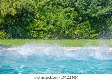 Big Splash Into Crystal Blue Waters Of A Garden Swimming Pool Surrounded By Green Lawn And Hedges, No People Visible