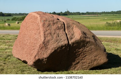 Big stone with split in lawn next to the road.