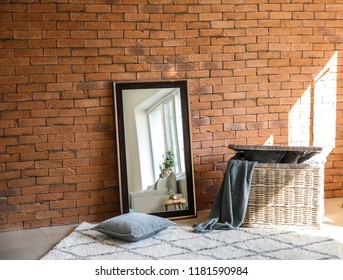 Big Stylish Mirror With Wicker Basket Near Brick Wall In Room