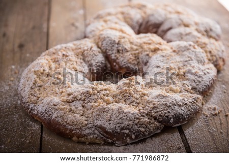 Big sweet kringle with butter crumbs and powdered sugar on wood table. A homemade dessert with a tasty and heartwarming look.