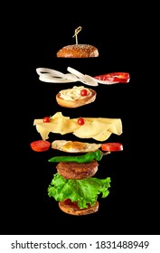 big tasty burger with meat cutlet, cheese, fried egg, tomatoes, cucumber pieces and green lettuce, fast food levitates, black background