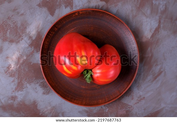 Big tomato of imperfect shape on clay\
plate. Top view. Homegrown produce. Ugly\
food