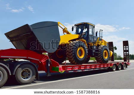 Big tractor machine heavy tool on truck transportation motion speed on road under blue sky