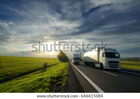 Big truck overtaking a small truck on a road in a rural landscape at sunset with dramatic clouds
