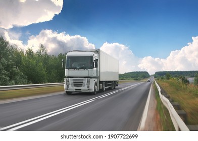 A big truck with a white trailer with space for text on a countryside road in motion against a blue sky with clouds