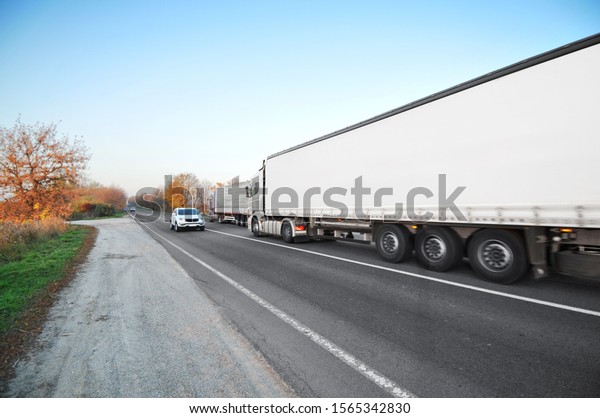 A big truck\
and white trailer with space for text and other vehicles on the\
countryside road against a blue\
sky