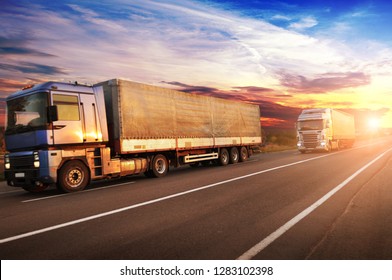 Big trucks and white trailers with space for text on the countryside road against sky with sunset