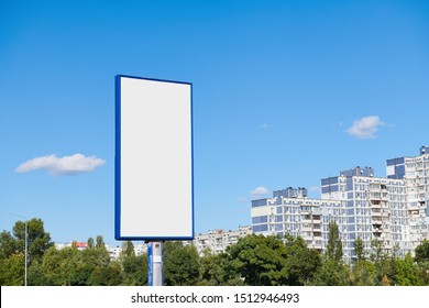 Big vertical billboard with copy space on urban background against blue sky. Advertising space with high-rise building and trees.