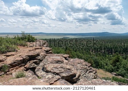 Big view from a rock ledge overlooking a forest and dry lakebed on a cloudy day.