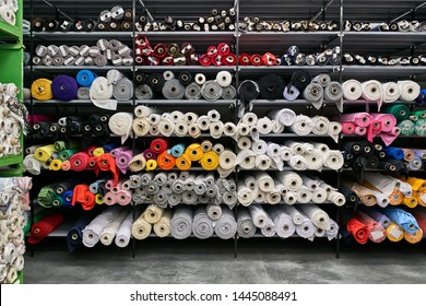 Big Warehouse With Many Shelves With Colorful Fabric Rolls On Them. They Are White, Gray, Black, Red, Pink, Orange, Blue, Cyan, Violet, Brown, Green And Beige. Horizontal.