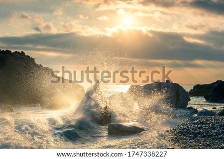 Big Wave hit the rock at beach, sea water splash up to the sky with sun. Sunset Sundown at Sea. Storm. Seascape.