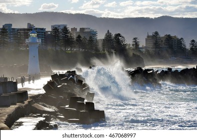 Big waves breaking over Wollongong harbor breakwall and lighthouse, Wollongong, New South Wales, Australia. People getting splashed by rough seas.