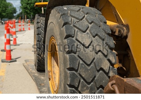 Big wheels on a front loader sitting idle in a road construction project are seen close up, emphasizing their size and power.