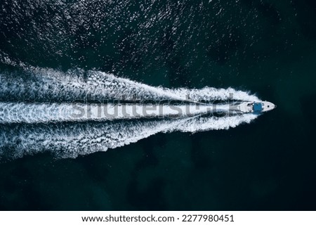 Big white boat with a blue awning fast movement on dark water top view.