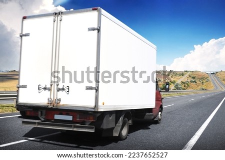 Big white box truck with a space for text on a highway road against a blue sky with clouds