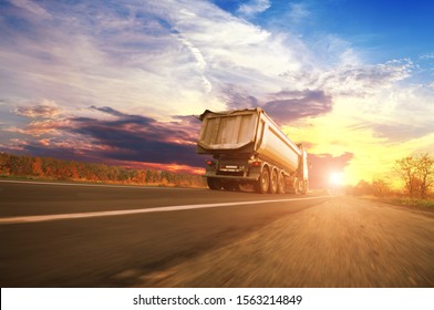 Big White Dump Truck In Motion On The Countryside Road Against A Night Sky With A Sunset