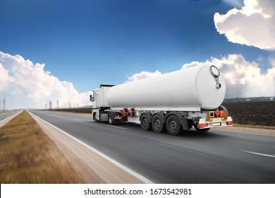 Big white fuel tanker truck shipping fuel on the countryside road in motion against blue sky with clouds