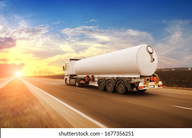 Big White Fuel Tanker Truck Shipping Fuel On The Countryside Road In Motion Against A Night Sky With A Sunset