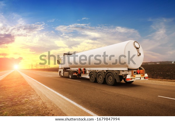Big white fuel tanker
truck shipping fuel on the countryside road against a night sky
with a sunset