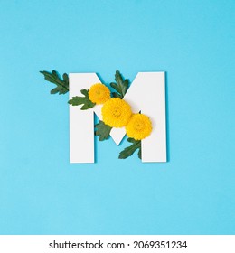 Big white Letter M made of real natural flowers and leaves on blue background. Flower font concept. Unique collection of letters. 