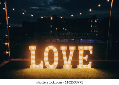 Big White Love Letters In Light Bulbs For Photo Booth At Wedding Reception In Night Outdoors. Love Word Lights, Stylish Evening Decor For Wedding Ceremony