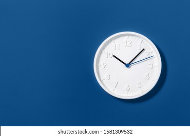 Big white plain wall clock on trending dark blue background. Ten o'clock. Close up with copy space, time management or school concept and summer standard or winter time change, opening hours.