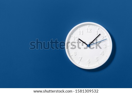 Big white plain wall clock on trending dark blue background. Ten o'clock. Close up with copy space, time management or school concept and summer standard or winter time change, opening hours.