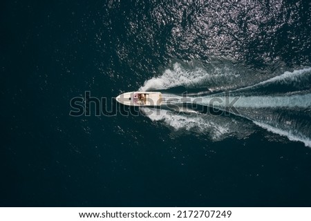 Big white speedboat moves fast on dark water top view. Big white boat with people moving on the water aerial view.
