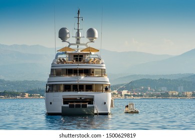 Big White Super Yacht, View From The Stern, Anchored In The Bay Of Cannes, France During Summertime With Open Umbrellas On The Top Deck For Entertainment Of Guests 