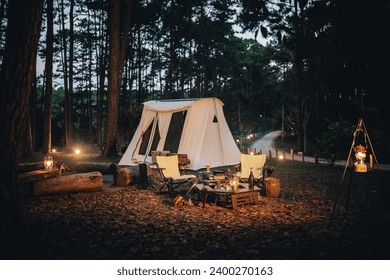 A big white tent in the woods with camping equipments and lanterns. Taken during an evening with dark sky. - Powered by Shutterstock