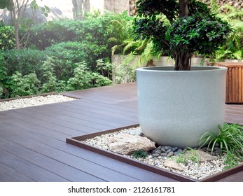 The big white terrazzo plant pot with a green tree on little stone garden space decoration on wood terrace near the green garden.