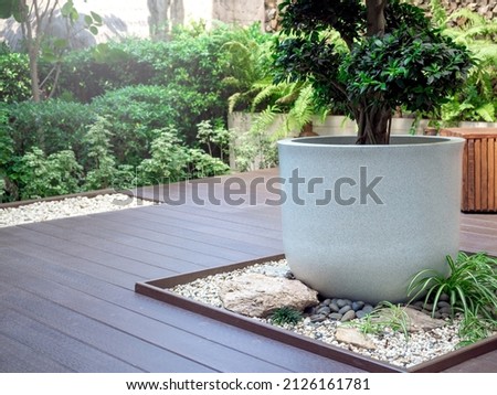 The big white terrazzo plant pot with a green tree on little stone garden space decoration on wood terrace near the green garden.