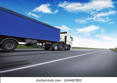 A big white truck and blue trailer with space for text on the countryside road in motion against a blue sky with clouds
