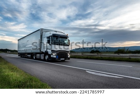Big White truck driving on the highway through countryside landscape at sunset.