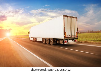 A Big White Truck And A Trailer With Space For Text On The Countryside Road In Motion Against A Night Sky With A Sunset