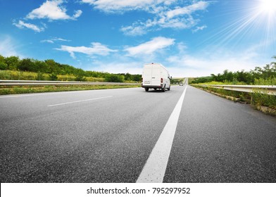 Big White Van On The Countryside Road Shipping Goods Against Blue Sky With Sun