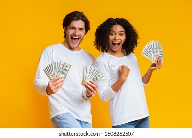 Big Win. Excited Interracial Couple Holding Lot Of Dollar Cash, Celebrating Success Together, Posing With Money Over Yellow Background, Free Space