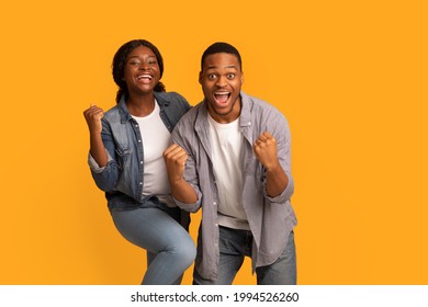 Big Win. Happy Excited Black Couple Celebrating Success With Raised Fists, Cheerful African American Man And Woman Exclaiming With Joy While Standing Isolated Over Yellow Background, Copy Space