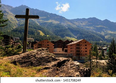 Big wooden cross with alpine village Zinal in the background on a bright sunny day in summer. Val d' Anniviers, Valais, Switzerland