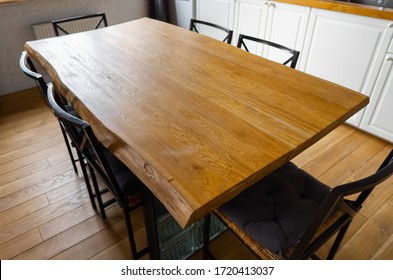 A big wooden dining table with glass blocks and metal wicker chairs and pillows in modern scandinavian an eat-in kitchen, against light wood floor, bright white furnitures and appliances - Shutterstock ID 1720413037