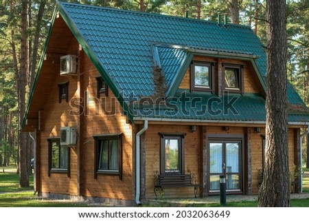 A big wooden house in the forest. Modern countryside wooden house with facade with big glass windows. Fir trees forest in the background.