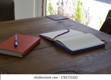 A big wooden table, red notebook, a pan and a leather brown backpack