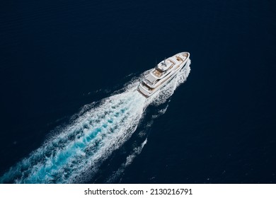 Big Yacht In The Sea Drone View. Luxury White Mega Yacht Fast Movement On Dark Water In The Ocean Top View. Big White Super Boat Moves On The Water Leaving A White Trail Aerial View.