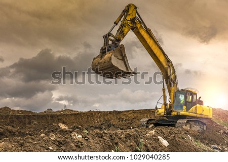 Big yellow digger on gravel heap with big shovel