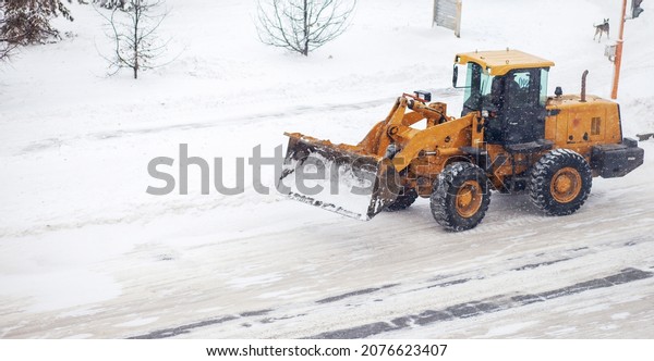 Big yellow tractor cleans up snow from the road\
and loads it into the truck. Cleaning and cleaning of roads in the\
city from snow in winter