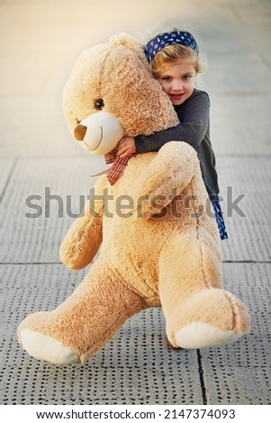 The bigger the bear, the bigger the cuddles. Portrait of a cute little girl holding an enormous teddybear while playing outside.